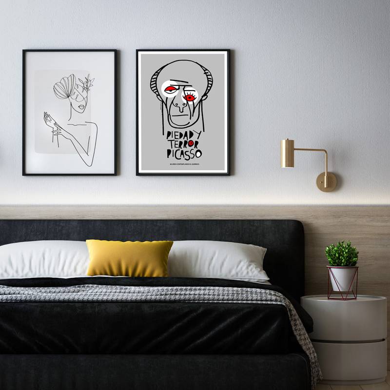 The minimalist graphic depicts Picasso’s face with red accent eyes, referencing the emotional power of ‘Guernica’. Displayed above a modern bed with monochrome bedding and a yellow accent pillow