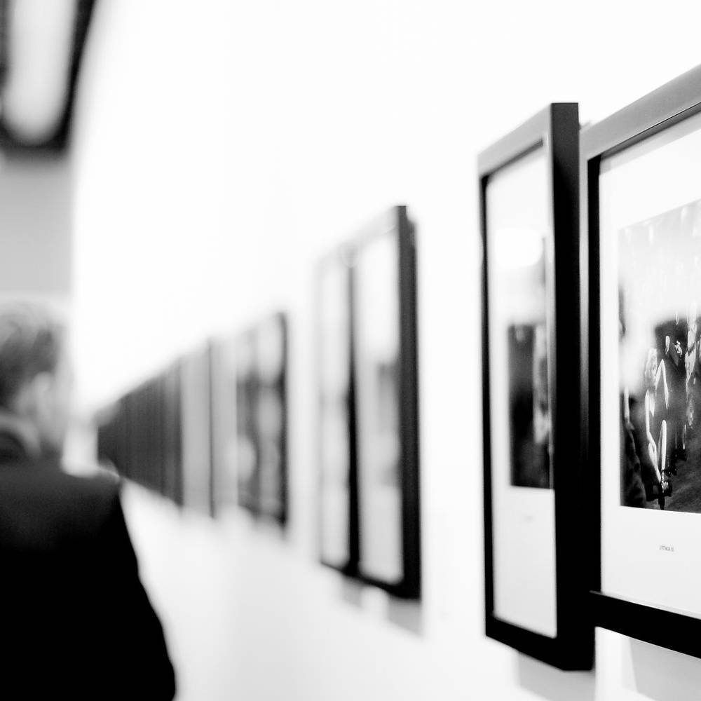 Visitors viewing a contemporary photography exhibition featuring framed black-and-white prints in a minimalist gallery setting